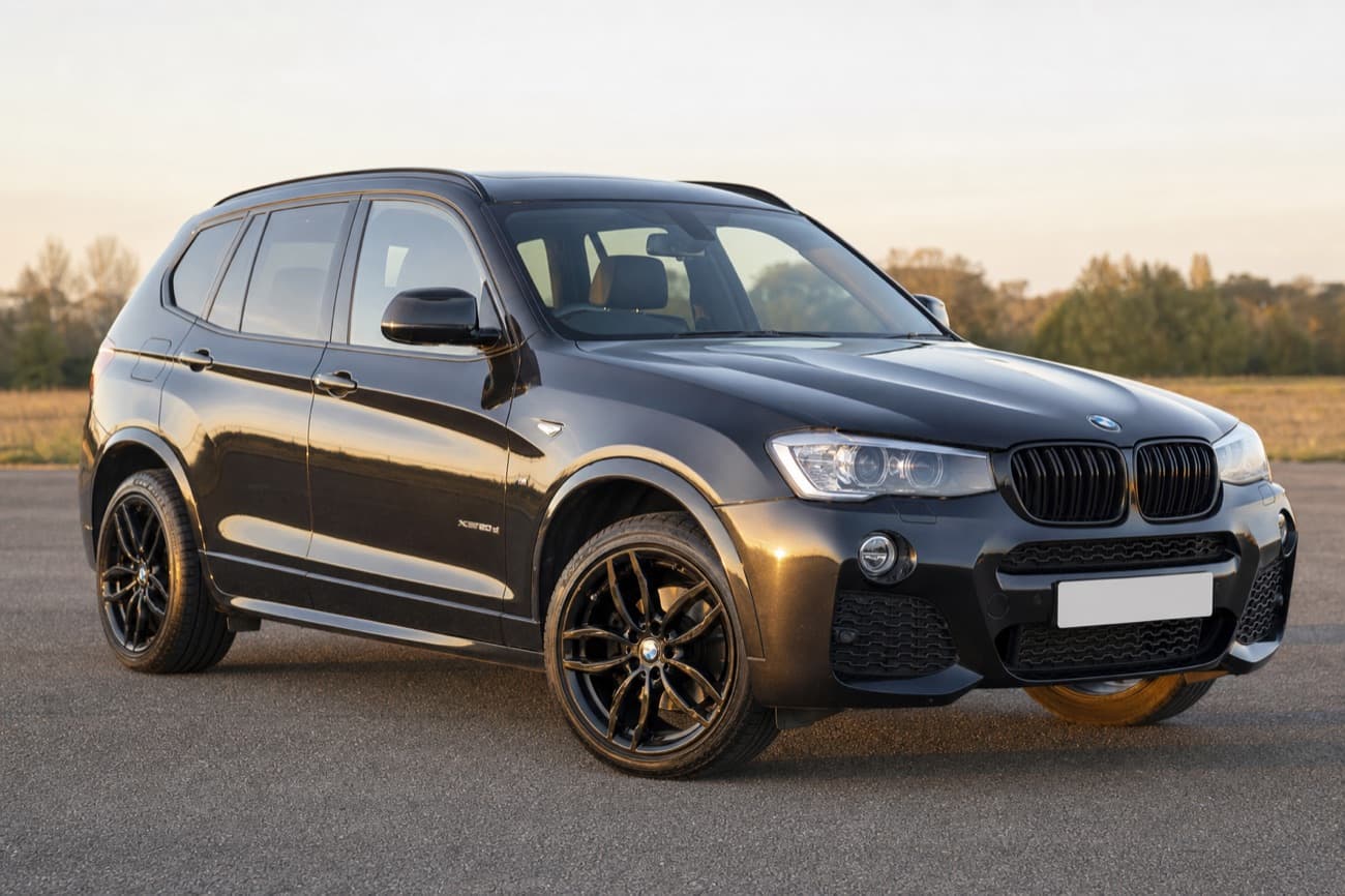 After: the same black BMW SUV alone at a three quarter front angle on clean tarmac in low evening light, plate blank