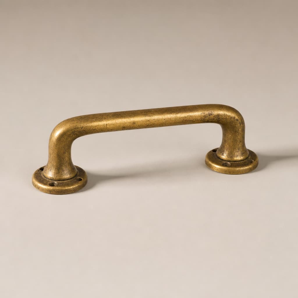 An old brass drawer handle on a plain warm grey background, one soft light from the upper left