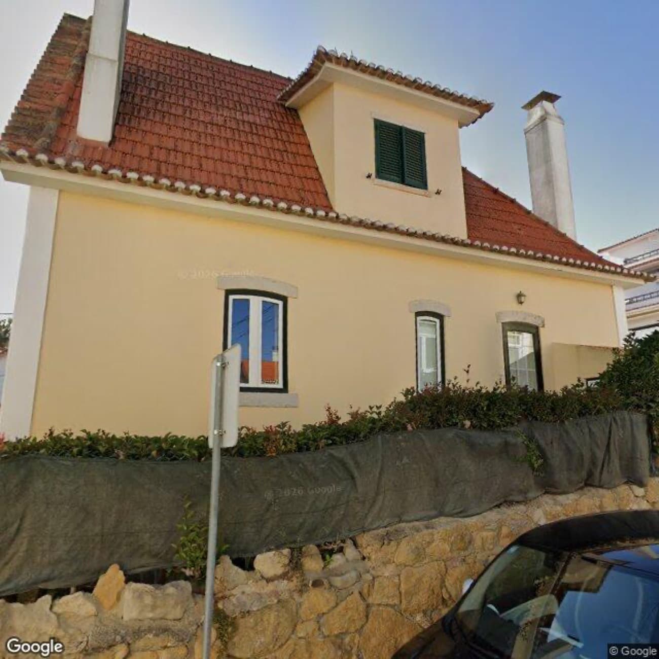 A Street View photo of a cream house behind a hedge, with a bare red tiled roof