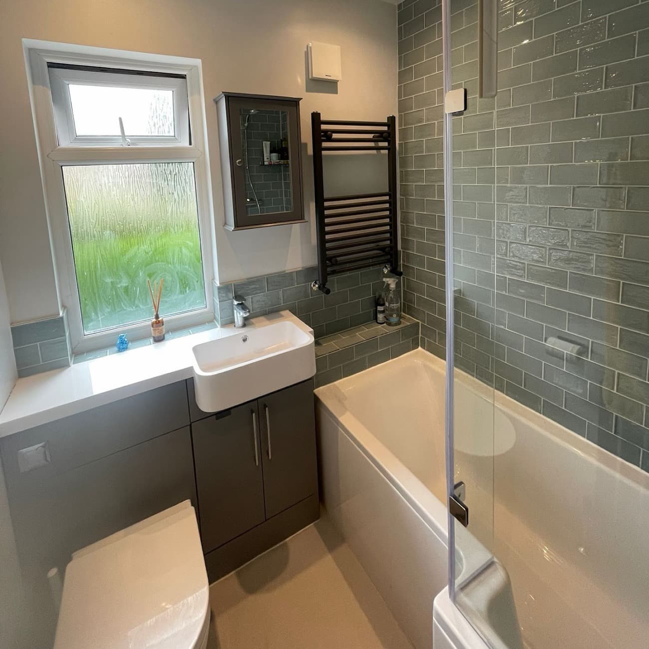 Before: a small grey-tiled bathroom lit by phone flash, walls leaning, cleaning spray on the shelf